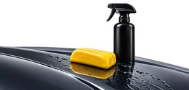 Detailing clay bar and lubricant beside a car paint panel